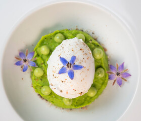 A fresh pea puree is beautifully plated, featuring a poached egg at the center and adorned with borage flowers. The dish showcases vibrant colors and textures, perfect for any spring menu.