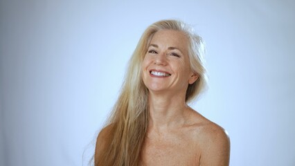 A mature woman smiles brightly in a spa setting, showcasing her joy and contentment. The soft white background adds to the tranquil ambiance during her relaxing moment.