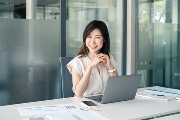 Obraz premium 30s middle-aged woman using computer technology for financial bank work online. Mature Asian professional it specialist businesswoman working on laptop pc sitting at desk in office. Portrait at camera