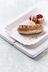 Grilled white sausage with ketchup on white paper tray. Rustic wooden background.	