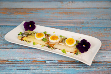 Baked asparagus with boiled egg in big white plate on blue background. High quality photo