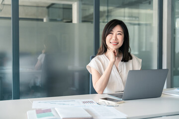 Thoughtful 30s middle-aged woman using computer for financial bank work online. Mature Asian professional specialist businesswoman working on laptop pc sitting at desk in office, looking at copy space