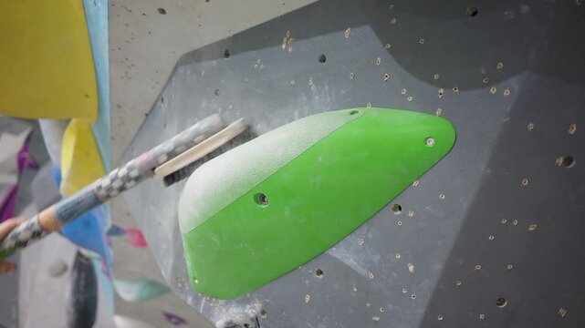 Hand holding big brush in bouldering climbing gym brushing off chalk of a large hold for the hands