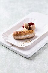Grilled white sausage with ketchup on white paper tray. Rustic wooden background.