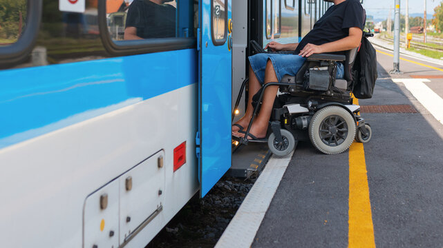 Man with disability using a wheelchair is at an accessible train station preparing to board a train. It is a sunny day, and the platform is designed for easy entry.