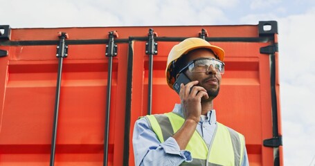 Portrait of focused successful African-American worker of transportation company talking on phone...