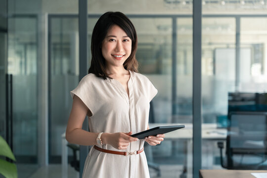 Fototapeta  Smiling entrepreneur businesswoman leader holding touchscreen pc device in office. Portrait at camera Asian mature woman ceo analyst manager using tablet for business work, learning or communication