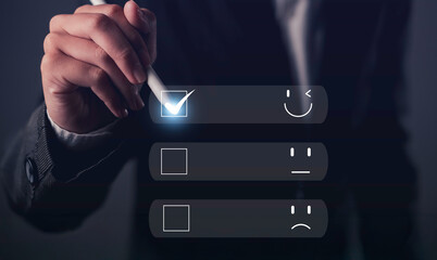 Hand holding stylus selecting happy face on digital satisfaction survey, representing positive feedback, customer experience, and user satisfaction.