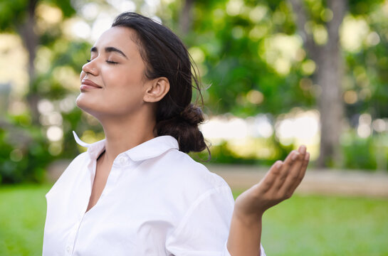 Positive relaxed happy refreshing young south asian woman taking a deep breath of clean unpolluted air in urban park, good summer, summer wellness, good sunlight exposure environment concept image