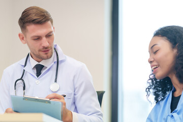 doctor in white gown with stethoscope,asking a woman patient on wheelchair a present illness and writing paper on clipboard to diagnosis and treatment