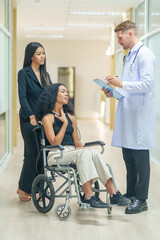 sick african business woman sitting on wheelchair at corridor with asian woman assistant,getting service at examine room in hospital