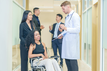 Fototapeta premium sick african business woman sitting on wheelchair at corridor with asian woman assistant,getting service at examine room in hospital