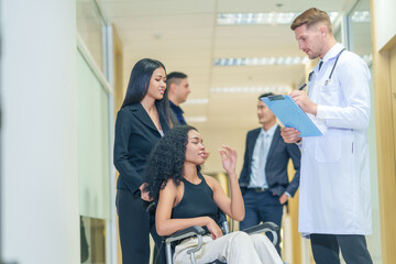 sick african business woman sitting on wheelchair at corridor with asian woman assistant,getting service at examine room in hospital