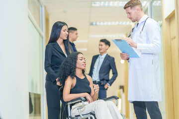 Obraz premium sick african business woman sitting on wheelchair at corridor with asian woman assistant,getting service at examine room in hospital