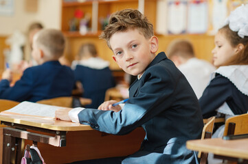 A first-grader boy is sitting at a desk in a classroom, the beginning of the school year. Back to...
