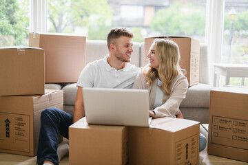 Young couple moving in new home. Couple is having fun with cardboard boxes in new house at moving...