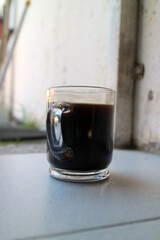a glass of black coffee in a glass cup photographed from the side, during the day