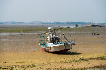 Small Fishing Boat on Tidal Flat with Coastal Village