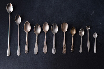 Set of different tea spoons. Silver cutlery on a black background. Spoon on the table top view