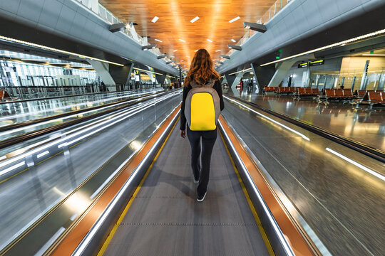 One woman traveller with backpack go on moving walkway travolator in new Hamad International Airport in Doha, Qatar. Back view of one person walks on travelator