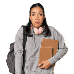 Young Filipino female student with books shrugs shoulders and open eyes confused.