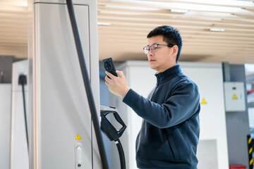 Male unplugging in power cord to electric car using app on smartphone