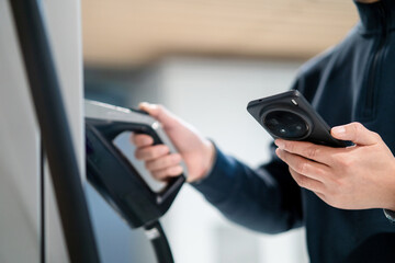 Male unplugging in power cord to electric car using app on smartphone