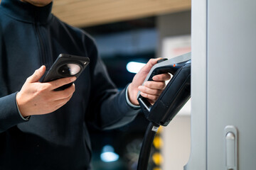 Male unplugging in power cord to electric car using app on smartphone