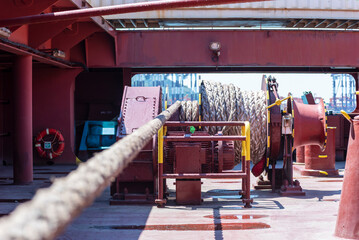 Large mooring winch on a ship's deck, featuring thick, braided ropes wound around a cylindrical metal drum. 