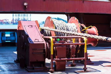 Large mooring winch on a ship's deck, featuring thick, braided ropes wound around a cylindrical metal drum. 