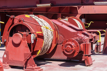 Large mooring winch on a ship's deck, featuring thick, braided ropes wound around a cylindrical metal drum. 