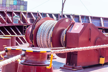 Large mooring winch on a ship's deck, featuring thick, braided ropes wound around a cylindrical metal drum. 
