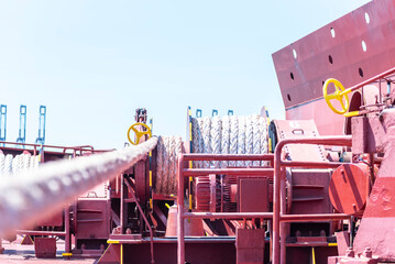 Large mooring winch on a ship's deck, featuring thick, braided ropes wound around a cylindrical metal drum. 