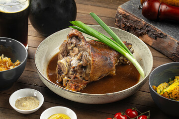 Portion of baked pork knuckle with sauce and spring onion