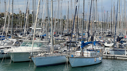 Sailboats docked in a marina under a cloudy sky.  Sailboats and yachts docked in a marina. Boats docked in a harbor under a cloudy sky. Barcelona