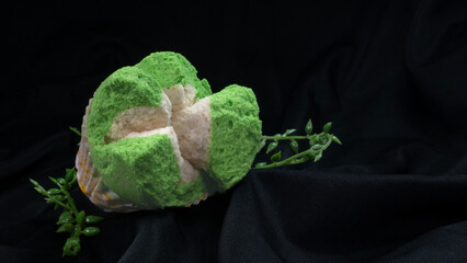A soft textured green blooming steamed sponge cake on black cloth and decorative leaves with dramatic light, suitable for advertising or promotion.