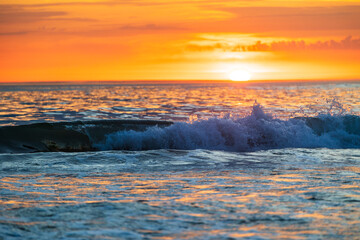 Wave on the ocean highlighted by the golden light of a sunset near the beach of La Parée in...
