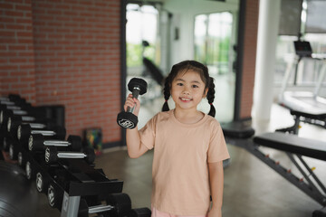 Young girl lifting dumbbell in fitness studio, promoting health and fitness for children, strong...