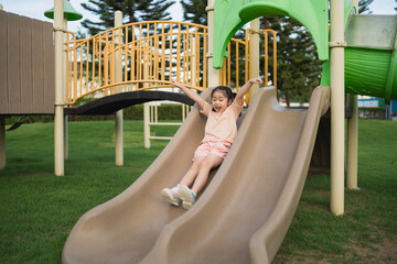 Excited child sliding down smooth slide at playground, enjoying outdoor fun and adventure on sunny day amidst green grass and playful environment