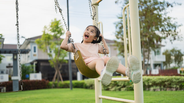 Joyful Child on Swing in Playground, Enjoying Sunny Day with Playful Expressions and Happy Mood Surrounded by Lush Green Grass and Garden