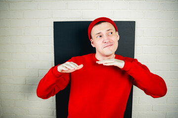 A man in a red hoodie and hat dances against a white brick wall