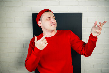 A man in a red hoodie and hat dances against a white brick wall