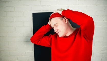 A man in a red hoodie and hat dances against a white brick wall