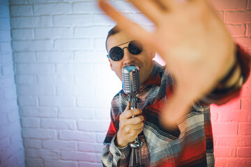 A man wearing a plaid shirt enthusiastically sings into a microphone, showcasing his passion for music and performance. He is fully engaged in the act of singing