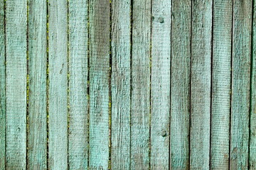 Old wooden boards stand close to each other to form a fence.