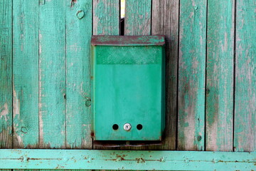 There is an old mailbox hanging on an old green fence.