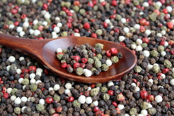 Wooden spoon with different types of peppercorns.	