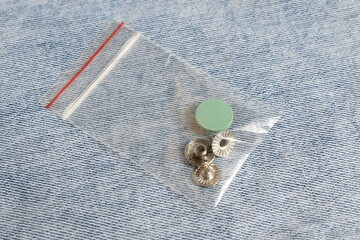 There is a disassembled iron button for jeans lying on the denim fabric.	