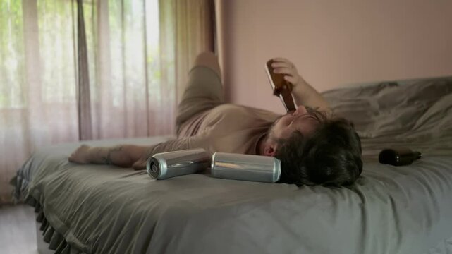 A man lies on a bed in despair, finishing a beer. Four empty bottles surround him, reflecting loneliness, alcohol abuse, or emotional breakdown at home.
