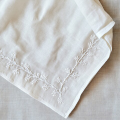 Embroidered white linen napkin on soft fabric. Minimal clean background for product presentation.